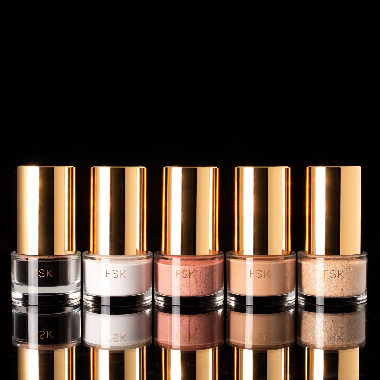 The FSK range under hot pink studio light, black bottle with a gold cap beside clear jars of acrylic powder
